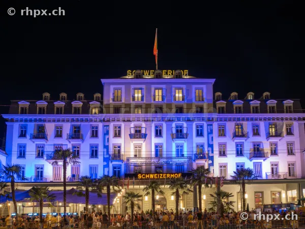 Fassade des Hotel Schweizerhof Luzern nachts blau beleuchtet mit Menschenmenge im Vordergrund