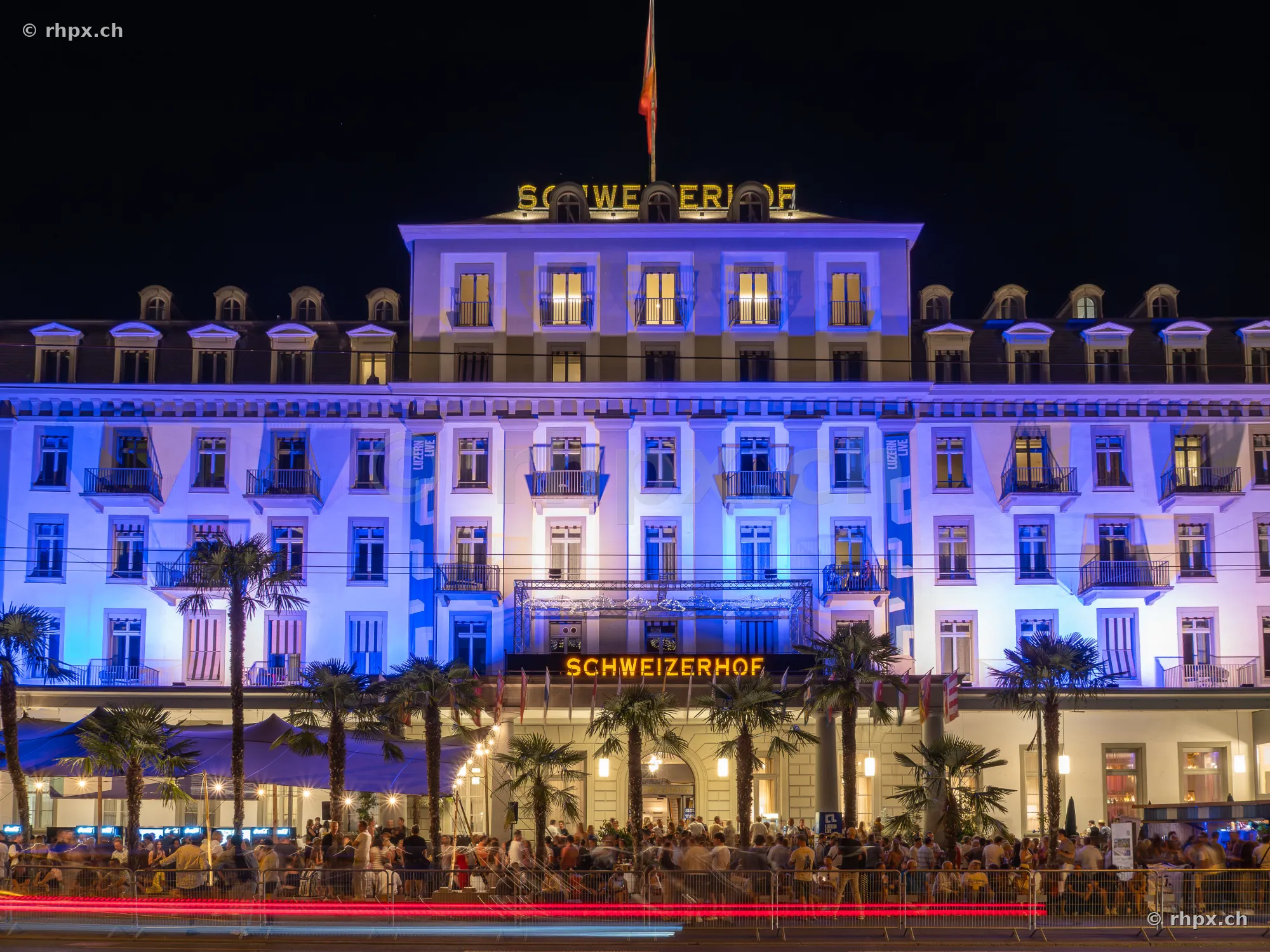 Fassade des Hotel Schweizerhof Luzern nachts blau beleuchtet mit Menschenmenge im Vordergrund