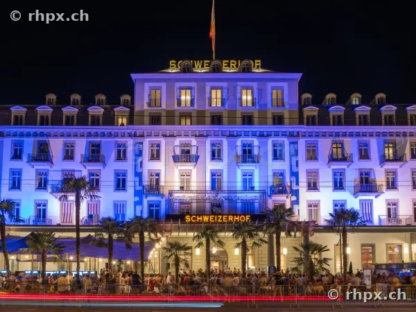 Fassade des Hotel Schweizerhof Luzern nachts blau beleuchtet mit Menschenmenge im Vordergrund