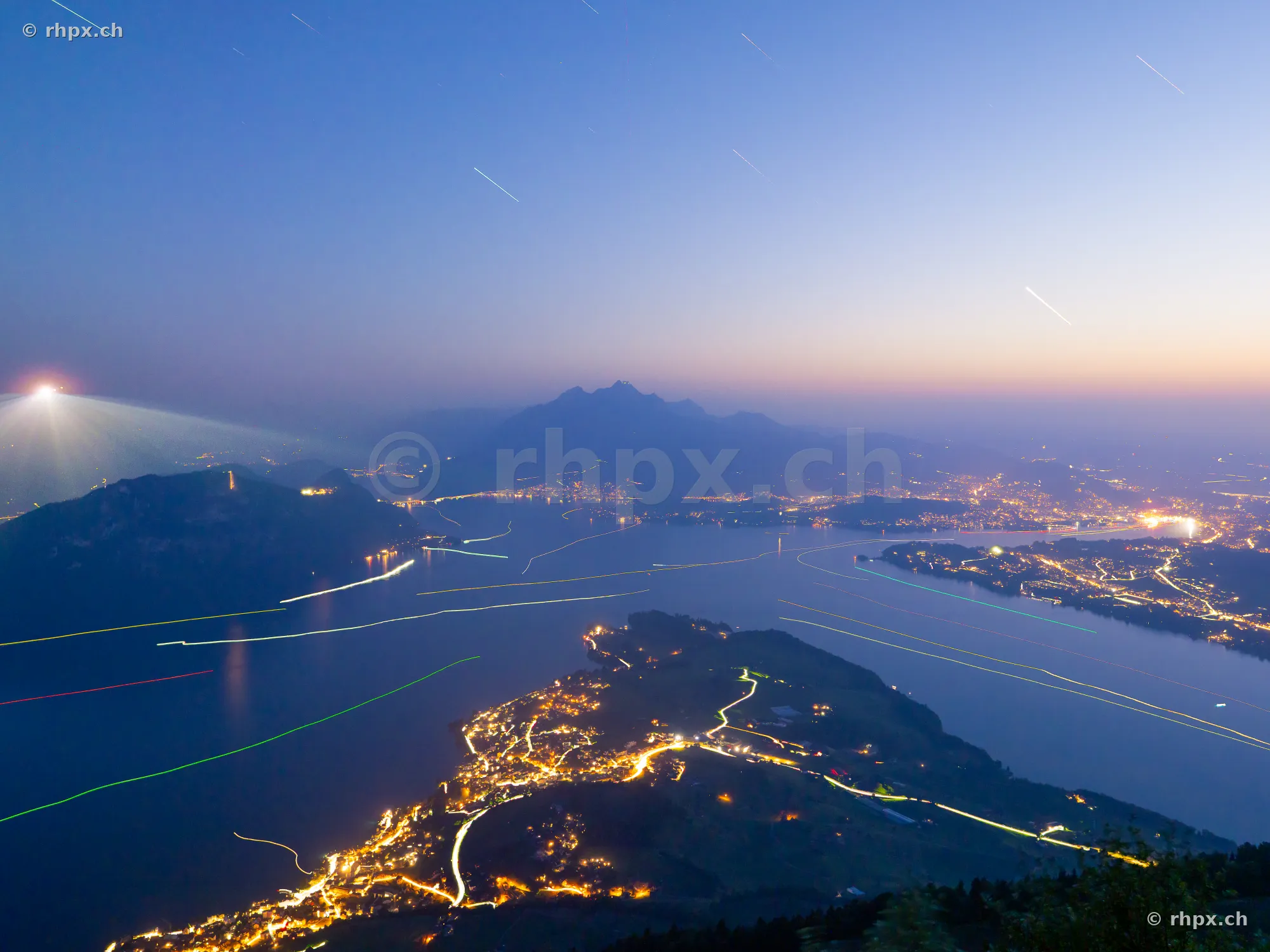 Night view of Lake Lucerne from above with light trails from ships and city lighting.