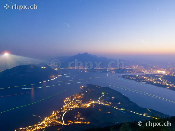 Night view of Lake Lucerne from above with light trails from ships and city lighting.