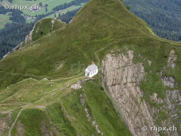 Aerial view of a small chapel on a green mountain ridge near Mount Pilatus