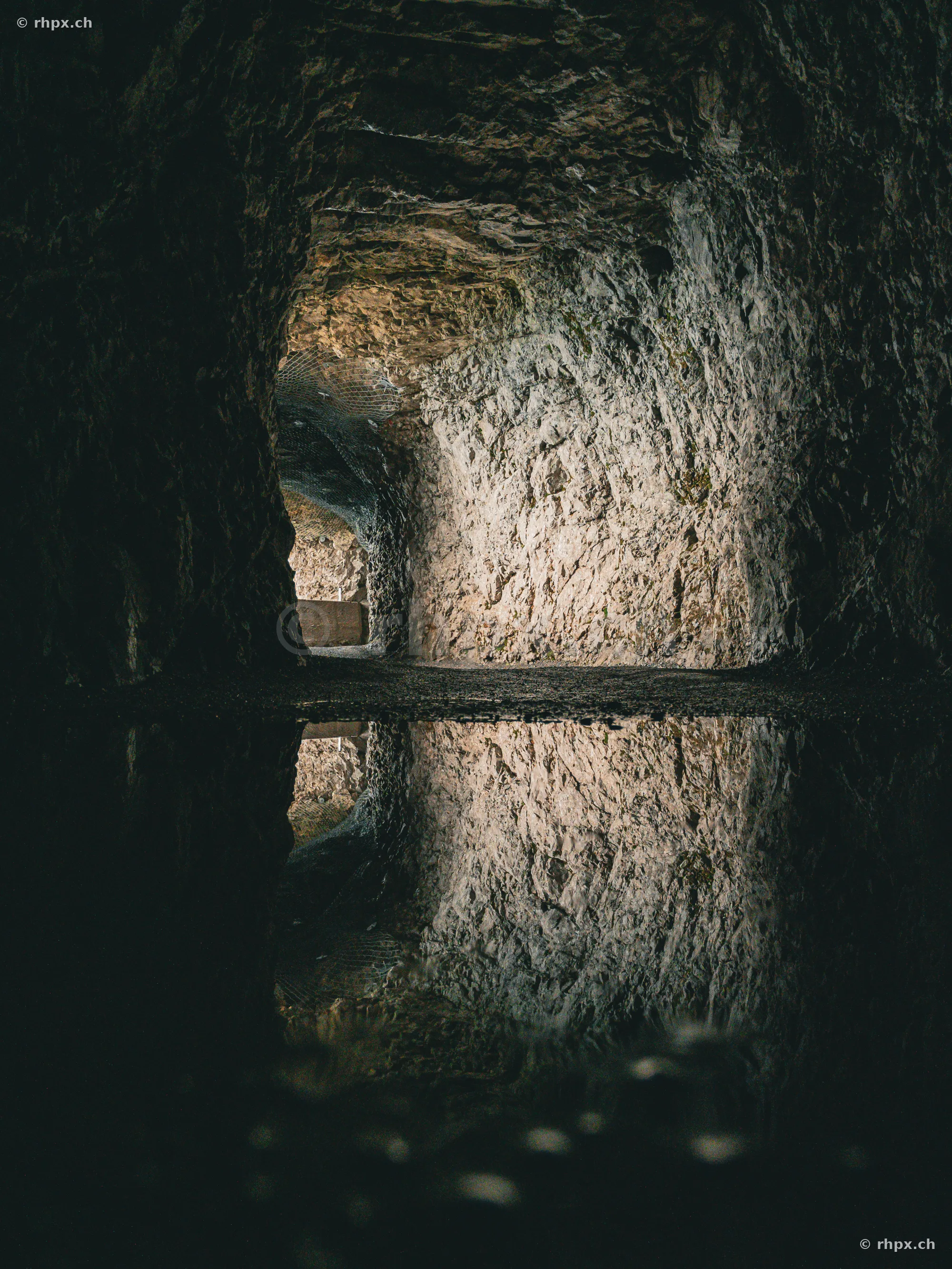 View through a rock tunnel at Mount Pilatus, reflected in a puddle on the ground