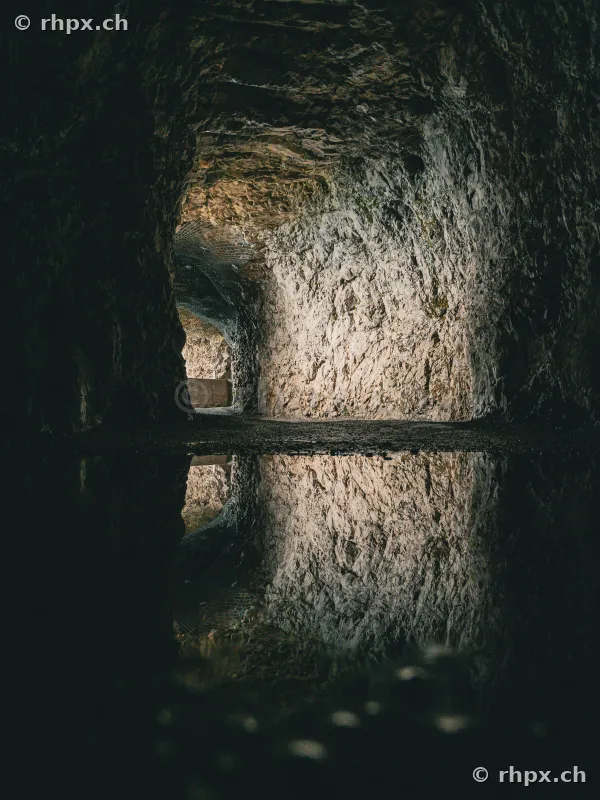 View through a rock tunnel at Mount Pilatus, reflected in a puddle on the ground