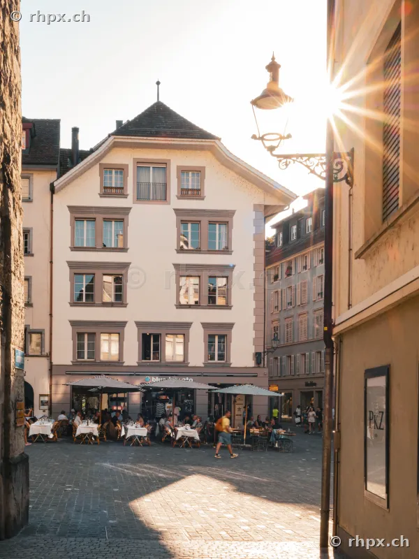 View of the streets at Weinmarkt in Lucerne's old town with restaurant terraces backlit by the sun