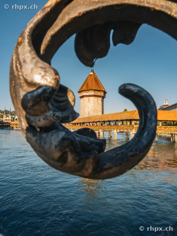 The Water Tower of the Chapel Bridge in Lucerne, seen through an ornamental wrought iron railing on the embankment.