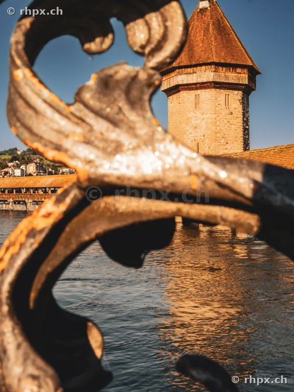View through a decorative metal railing towards the Wasserturm of the Chapel Bridge in Lucerne.