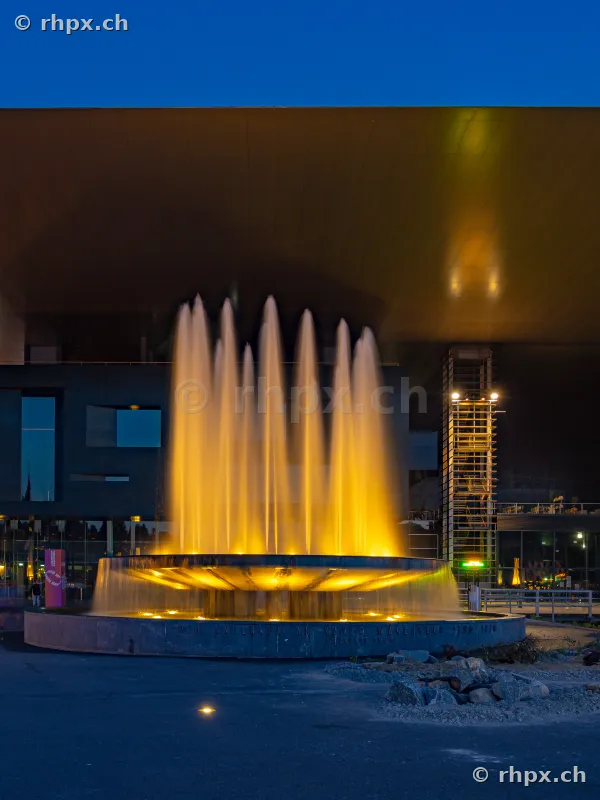 Illuminated fountain in front of the facade of the KKL Culture and Convention Centre Lucerne at twilight