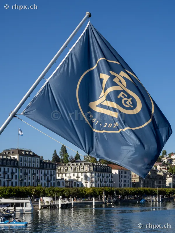 A dark blue anniversary flag of FC Luzern blowing in front of the Lucerne lakeshore scenery.