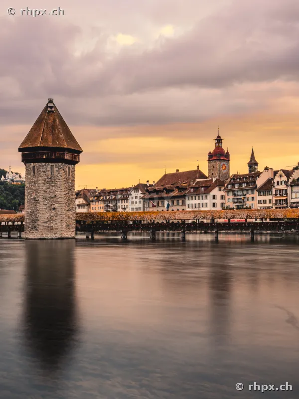 Water tower and Chapel Bridge in Lucerne with the silhouette of the old town in evening light