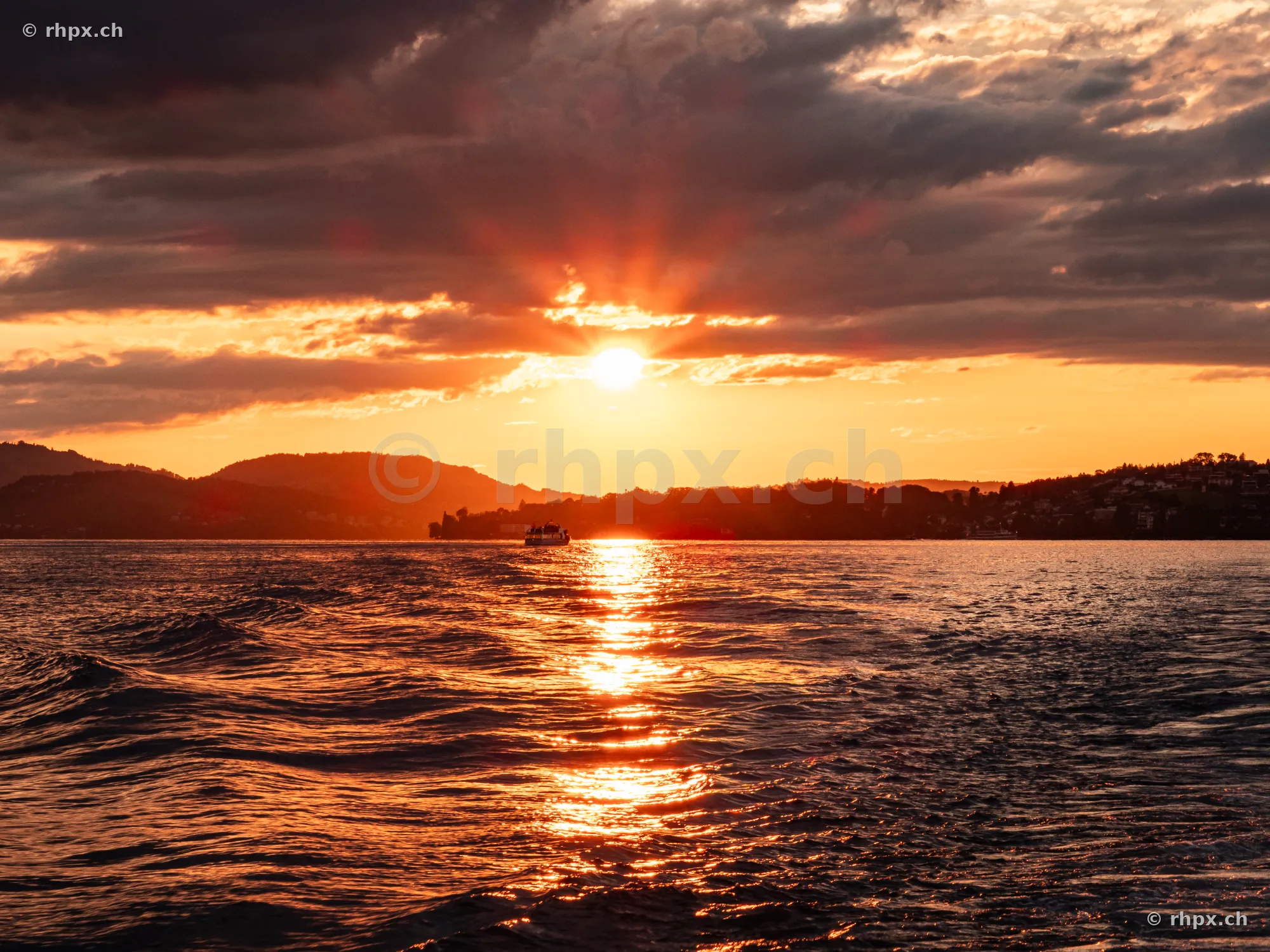 Orange sunset over Lake Lucerne with a small ship on the horizon
