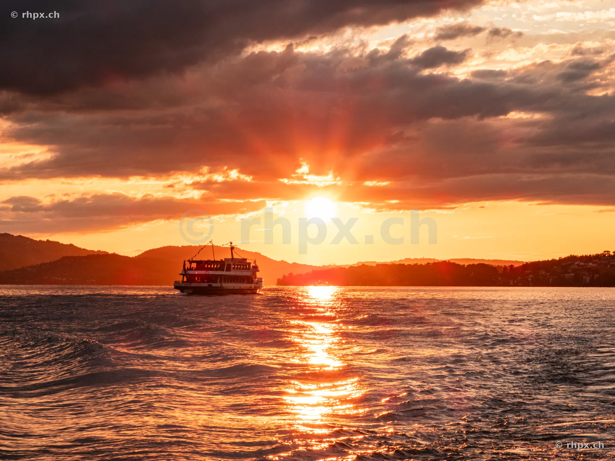 A passenger ship cruising on Lake Lucerne during an orange sunset