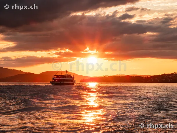 A passenger ship cruising on Lake Lucerne during an orange sunset