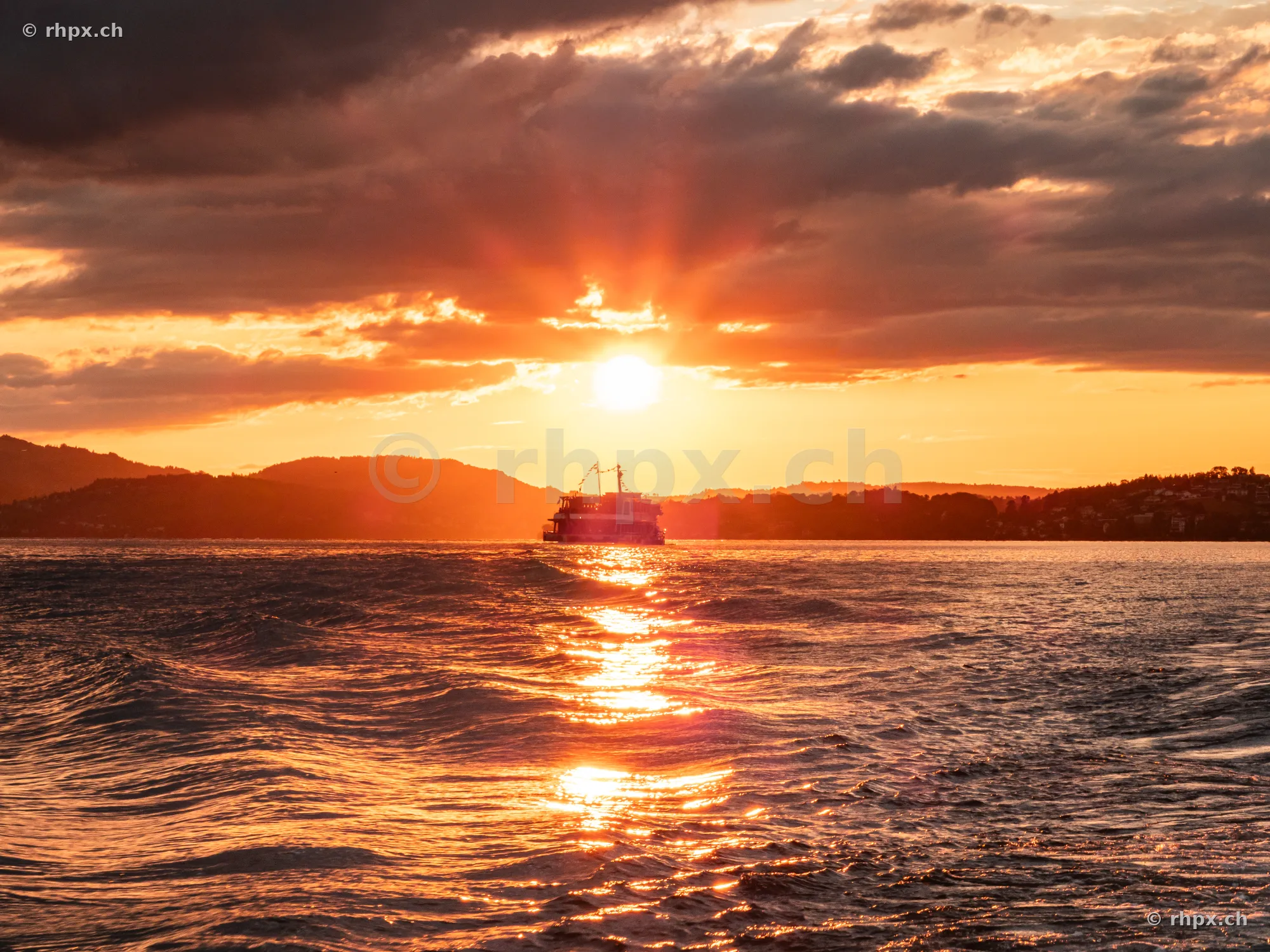 A ship sailing on Lake Lucerne during an orange sunset