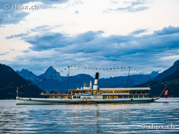 The paddle steamer Uri cruising on Lake Lucerne at dusk in front of a mountain landscape