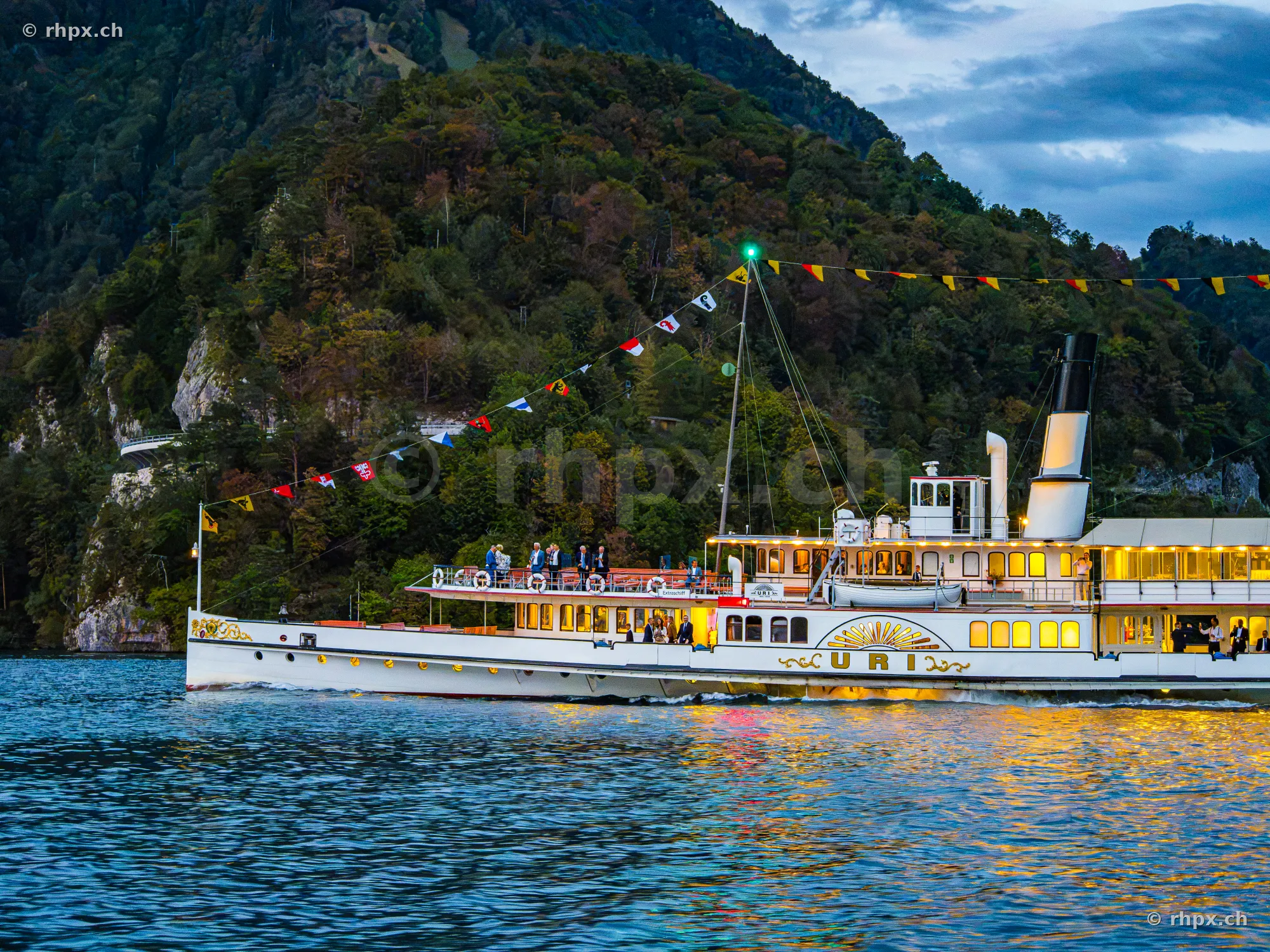 Illuminated paddle steamer Uri on Lake Lucerne with a forested mountain backdrop