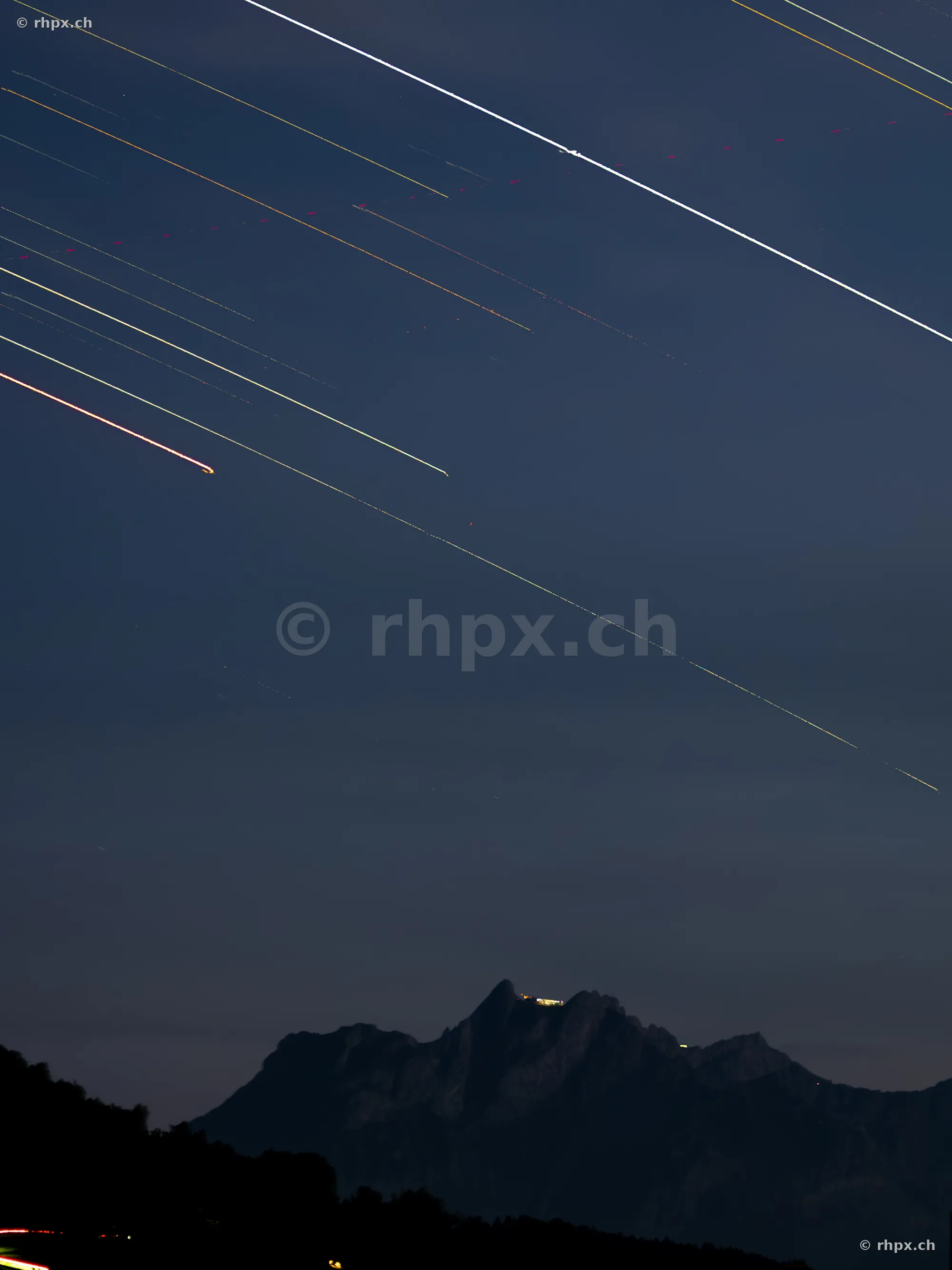 Dark night sky with airplane light trails above the Pilatus massif