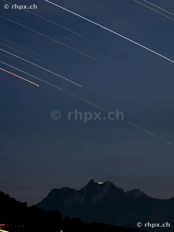 Dark night sky with airplane light trails above the Pilatus massif