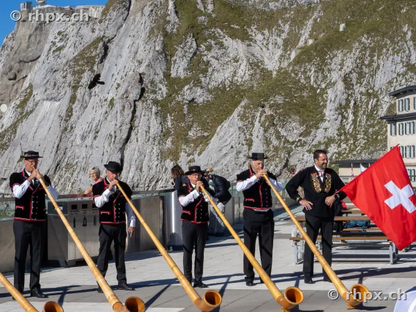 Group of alphorn players in traditional Swiss costume in front of the Pilatus rock face