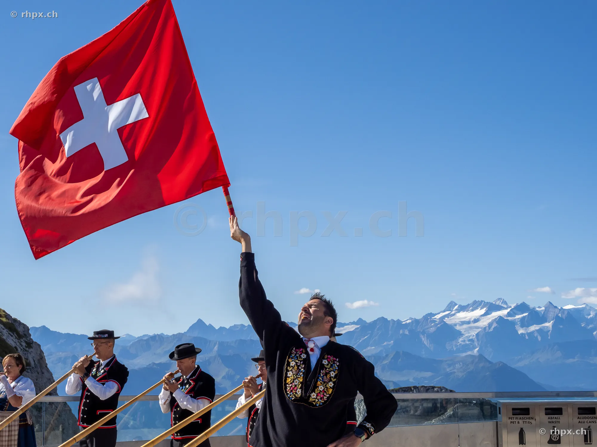 A man swinging a Swiss flag in front of the mountain panorama on Mount Pilatus