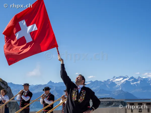 A man swinging a Swiss flag in front of the mountain panorama on Mount Pilatus