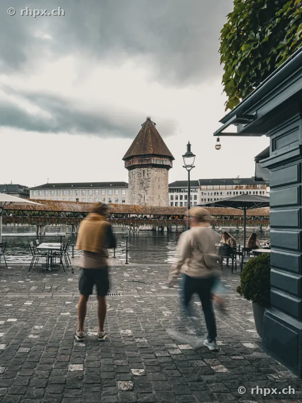 View of the Wasserturm and Chapel Bridge in Lucerne with pedestrians on the cobbled forecourt