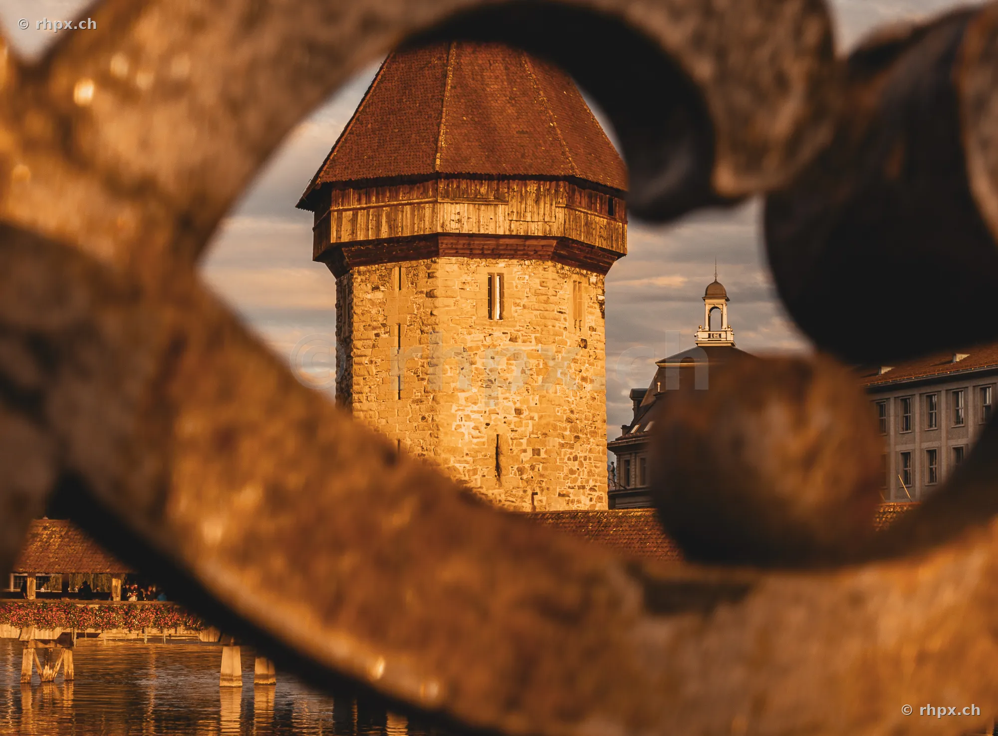 Wasserturm in Luzern im goldenen Licht durch ein verschwommenes Geländer im Vordergrund betrachtet