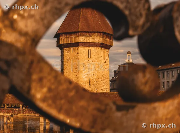 Wasserturm in Luzern im goldenen Licht durch ein verschwommenes Geländer im Vordergrund betrachtet