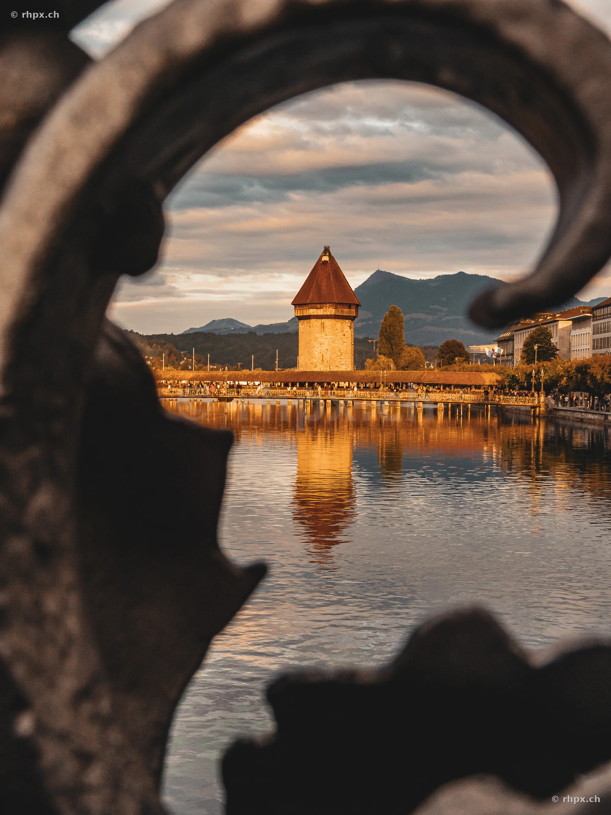 Blick durch ein verziertes Eisengeländer auf die Kapellbrücke und den Wasserturm in Luzern bei Abendlicht