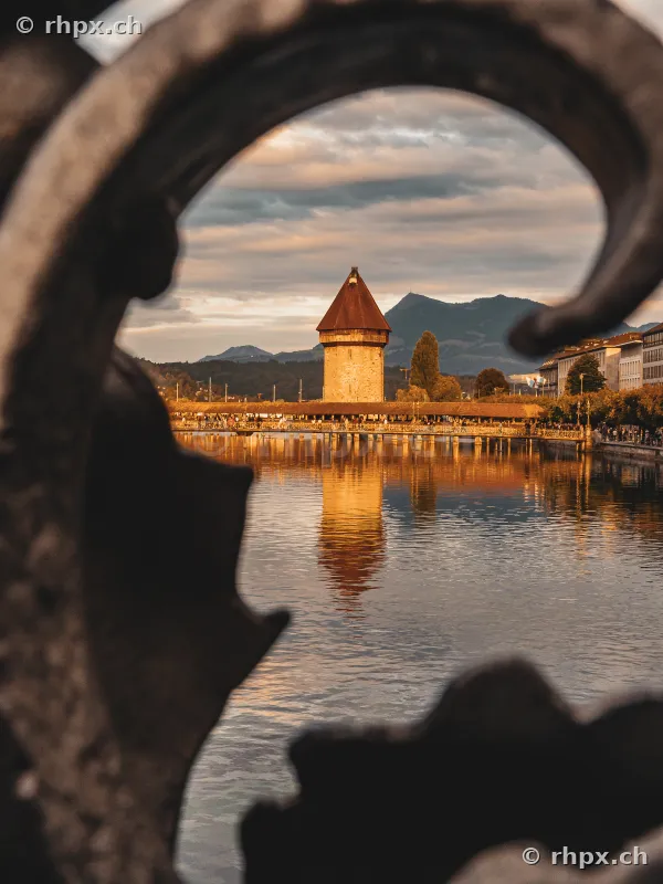 Blick durch ein verziertes Eisengeländer auf die Kapellbrücke und den Wasserturm in Luzern bei Abendlicht
