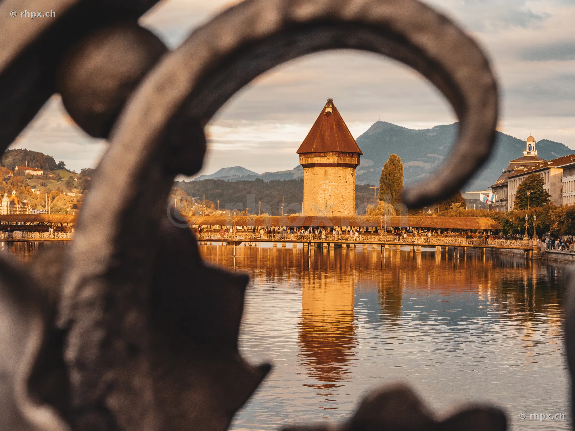 Blick auf den Wasserturm und die Kapellbrücke in Luzern durch ein verziertes Eisengeländer