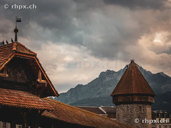 Kapellbrücke und Wasserturm in Luzern mit dem Pilatus im Hintergrund unter dunklen Gewitterwolken.