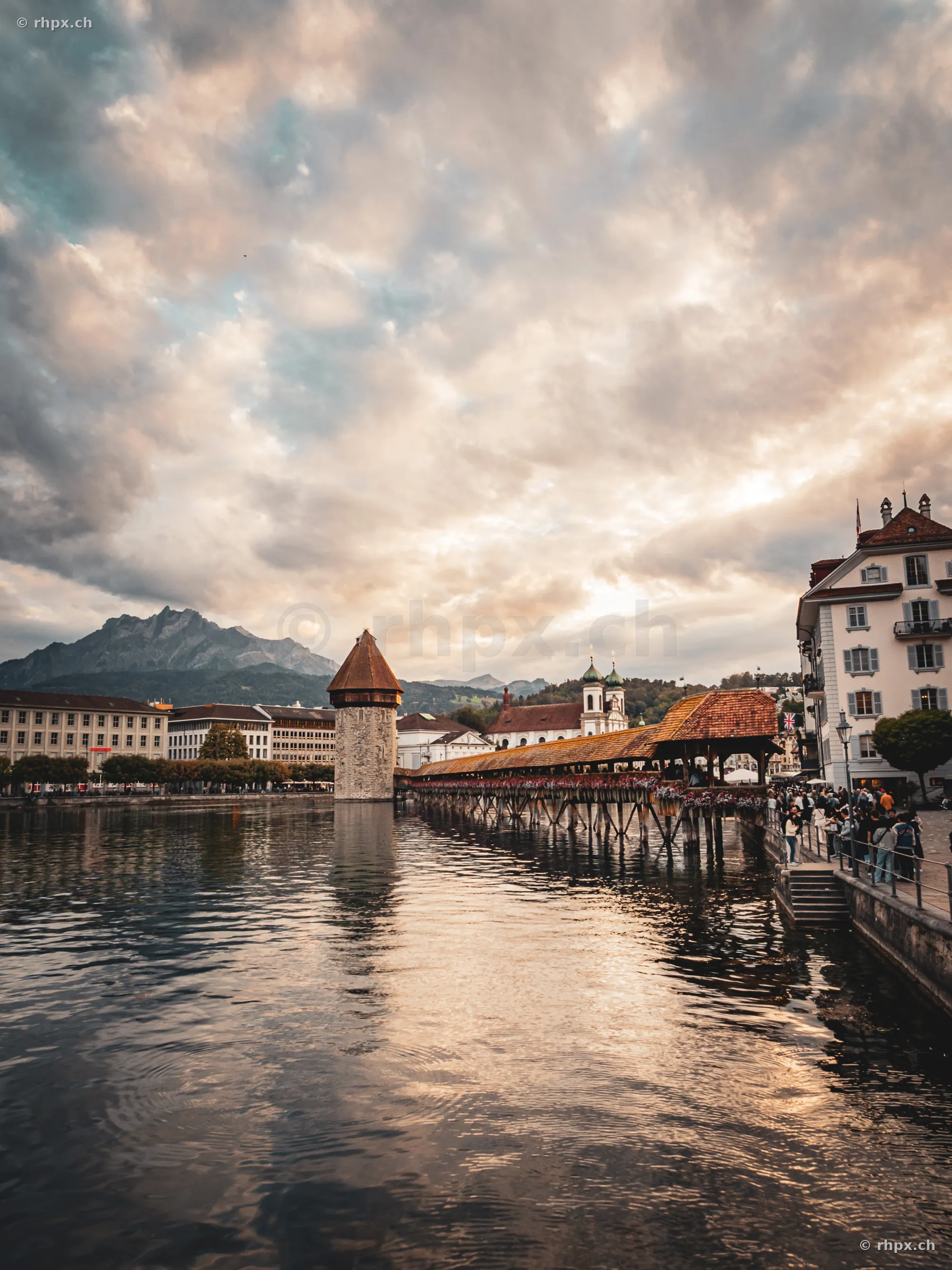 Blick auf die Kapellbrücke mit Wasserturm und Pilatus im Hintergrund bei bewölktem Abendhimmel