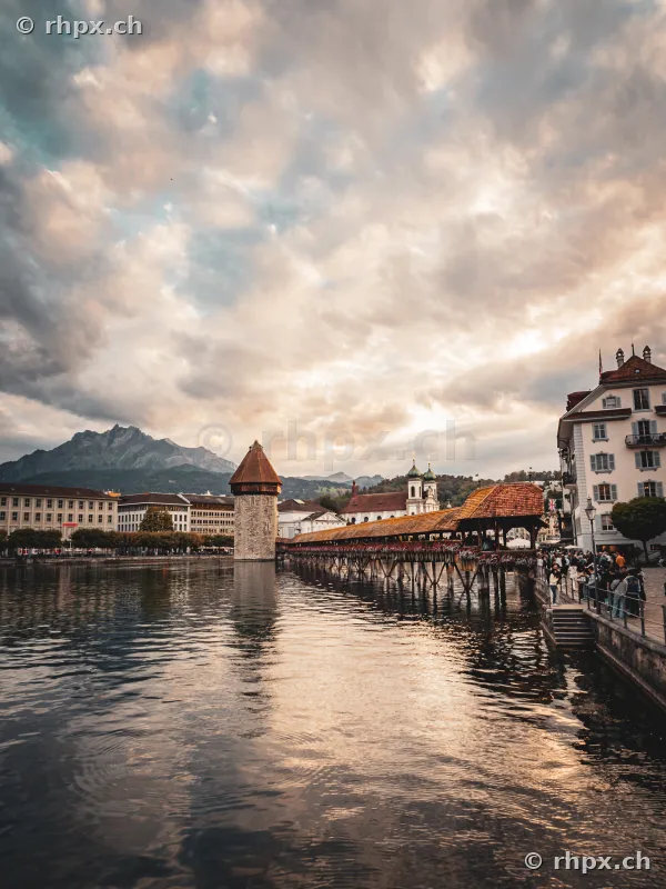 Blick auf die Kapellbrücke mit Wasserturm und Pilatus im Hintergrund bei bewölktem Abendhimmel