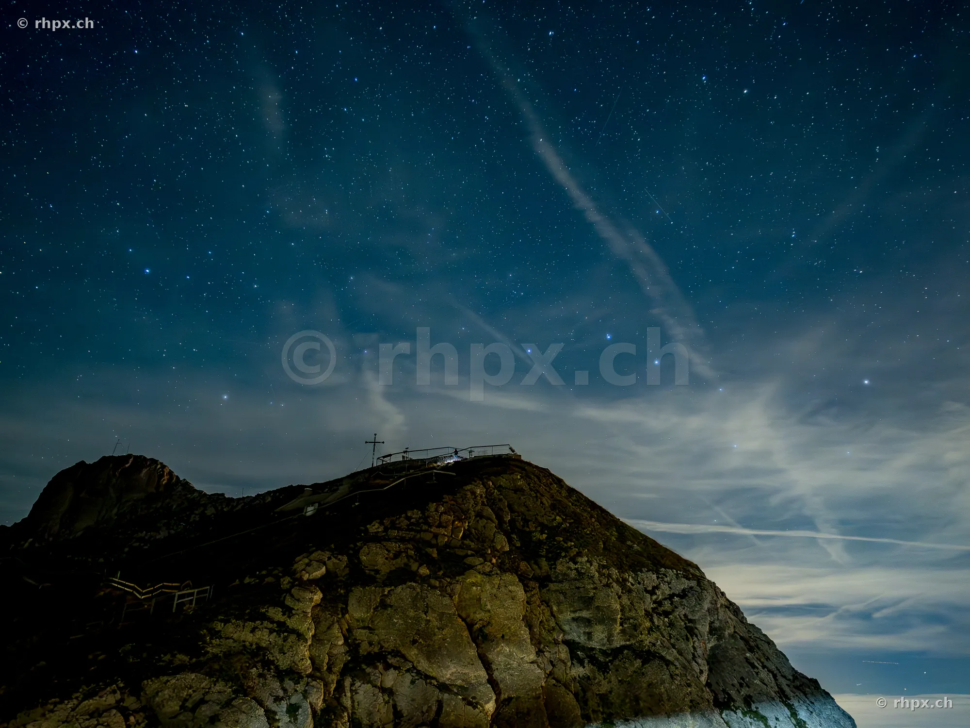 Rocky summit of Mount Pilatus at night with a starry sky and a summit cross