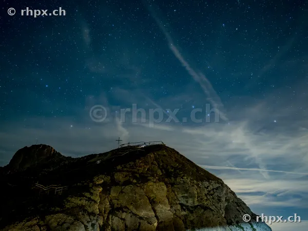 Rocky summit of Mount Pilatus at night with a starry sky and a summit cross