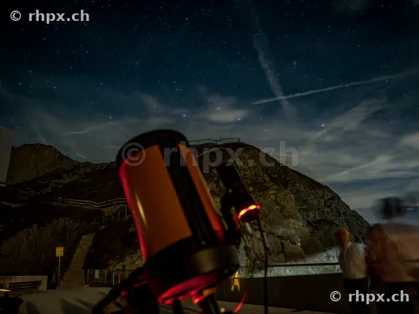 View of a telescope in front of Mount Pilatus at night with a starry sky