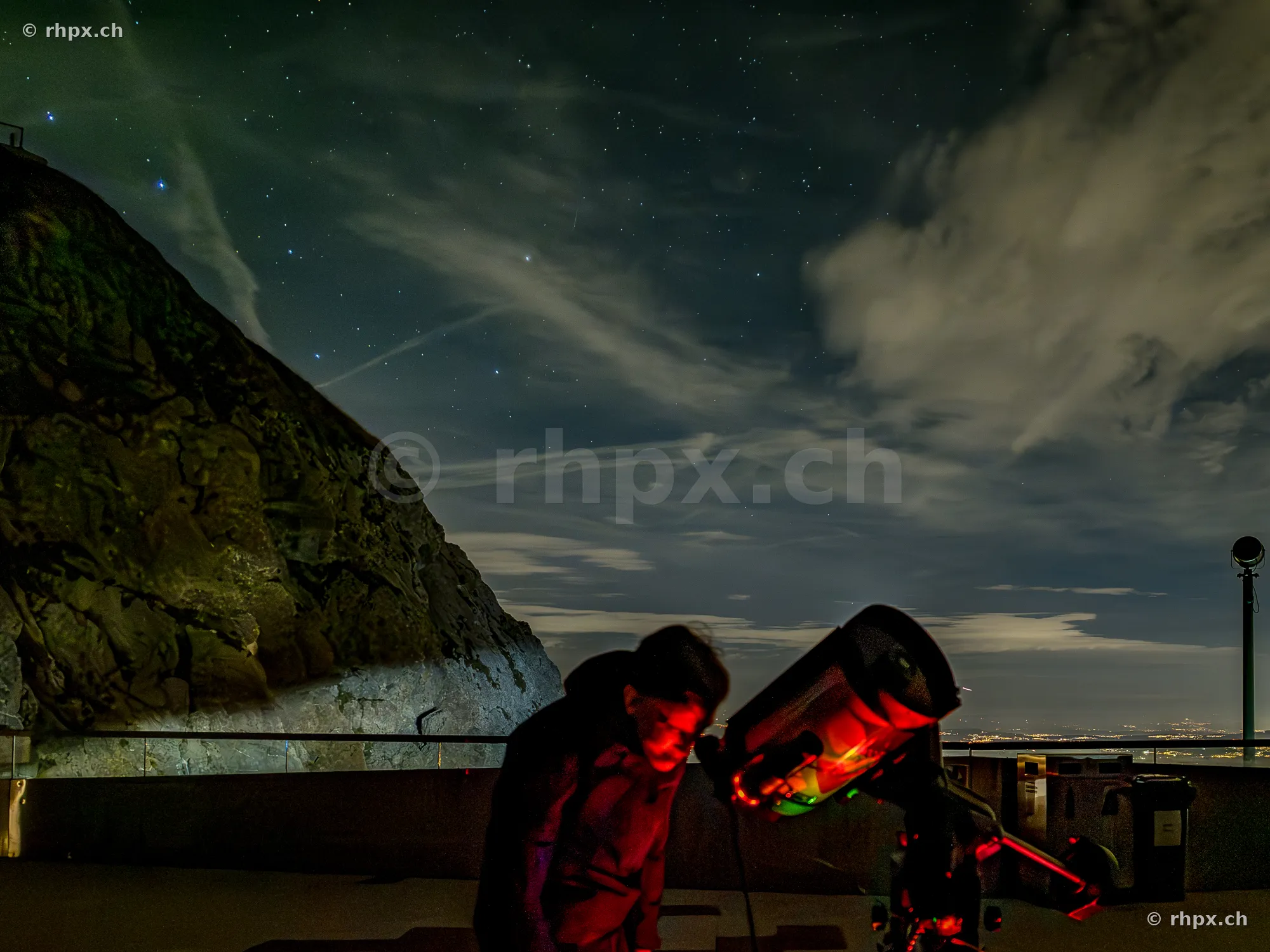 Person looking through a telescope at night on the peak of Mount Pilatus