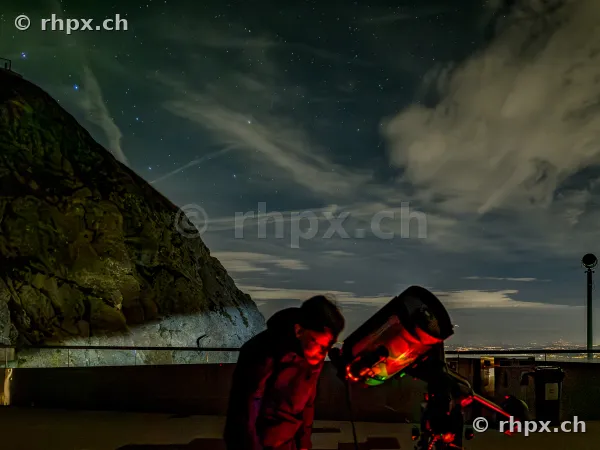 Person looking through a telescope at night on the peak of Mount Pilatus