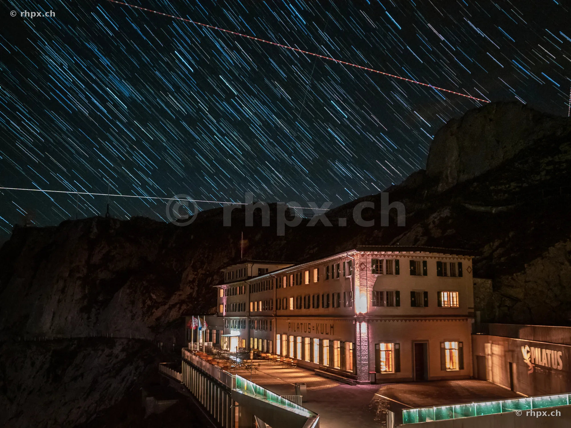 Long exposure of nocturnal star trails above the illuminated Hotel Pilatus Kulm