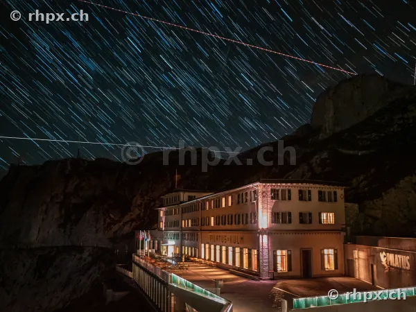 Langzeitbelichtung der nächtlichen Sternspuren über dem beleuchteten Hotel Pilatus Kulm