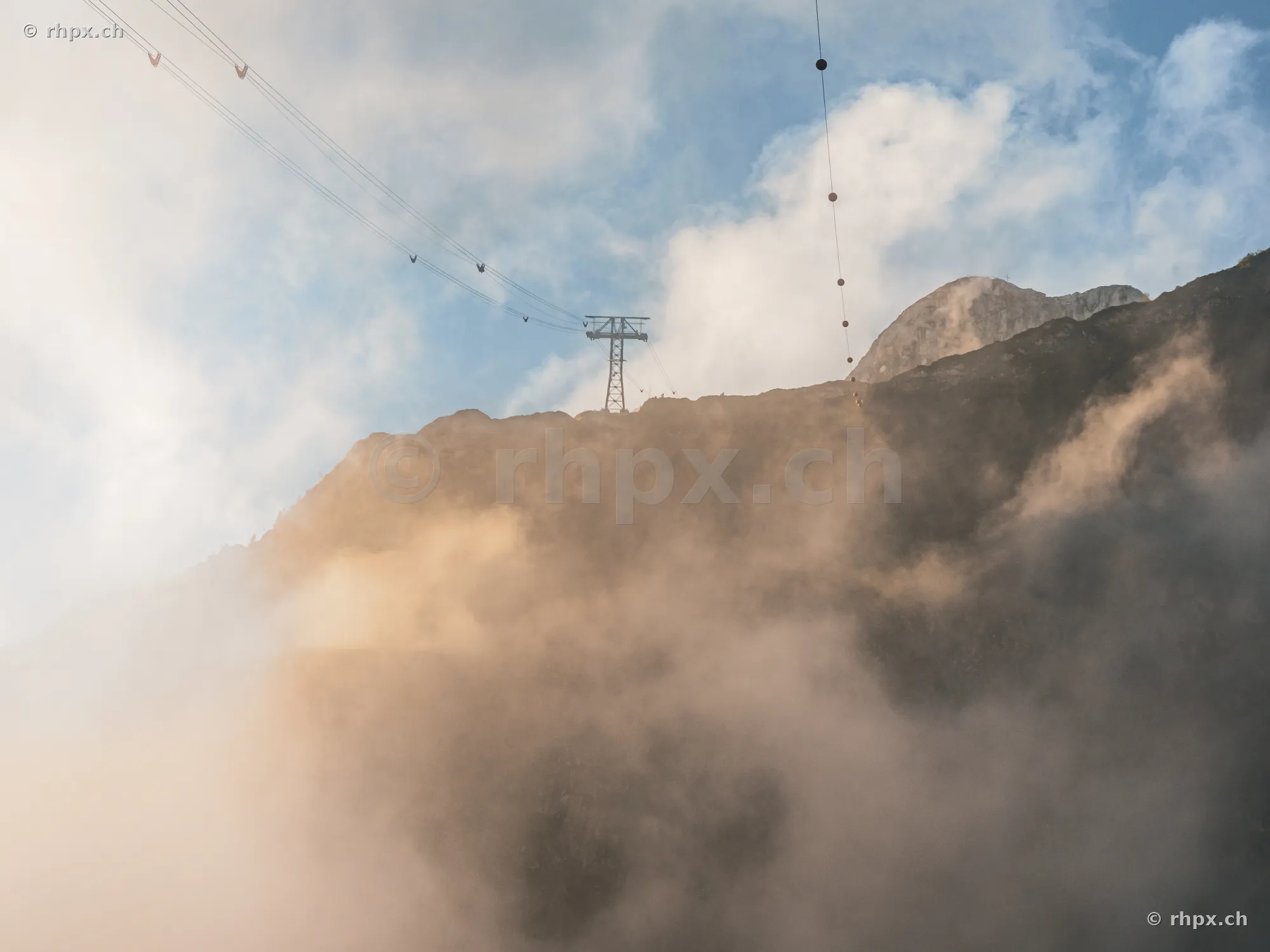 Aerial cableway pylon on the rocky slope of Mount Pilatus, surrounded by clouds and fog.