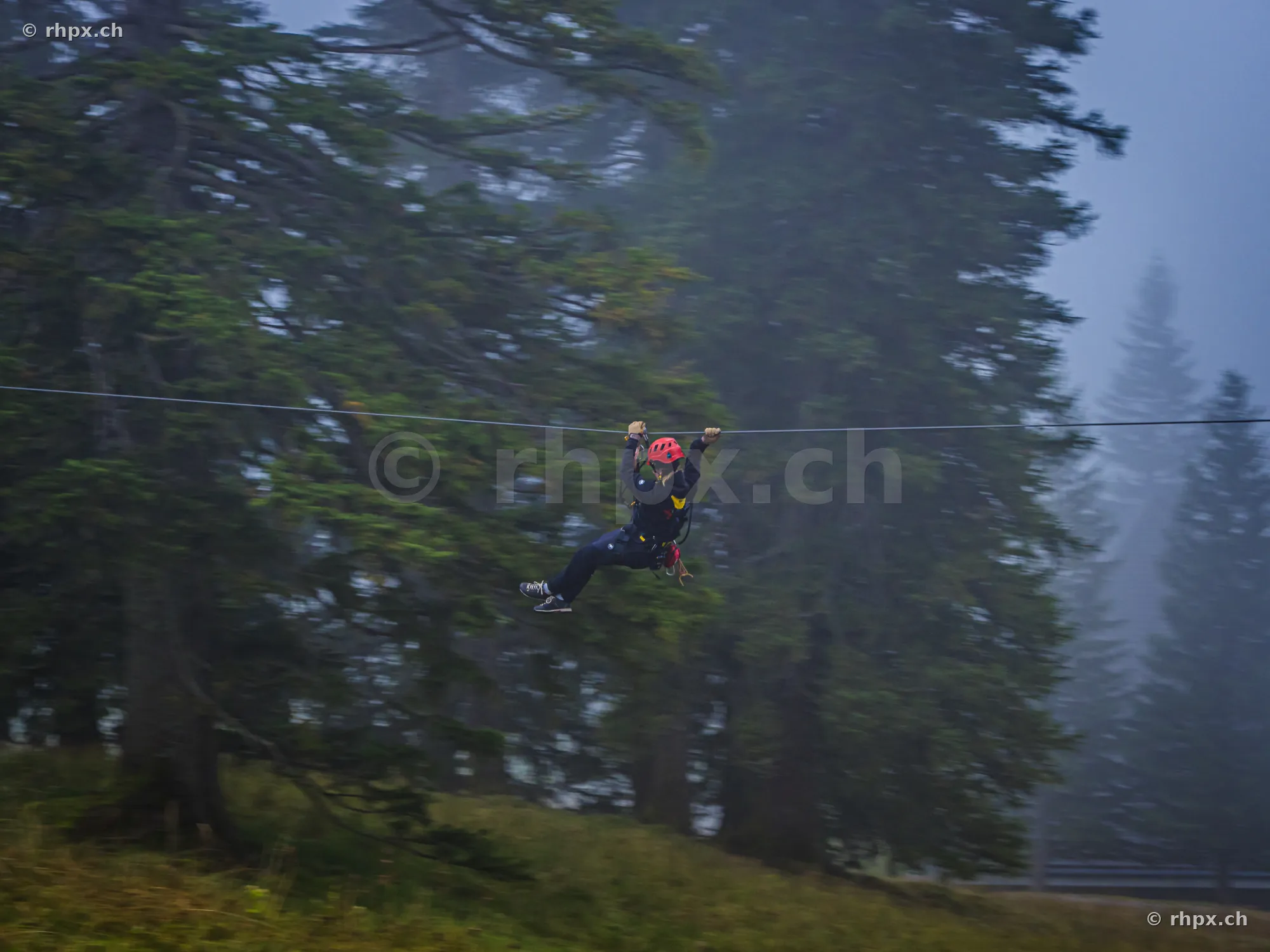 Person in Schutzausrüstung an einer Seilrutsche im nebligen Wald am Pilatus