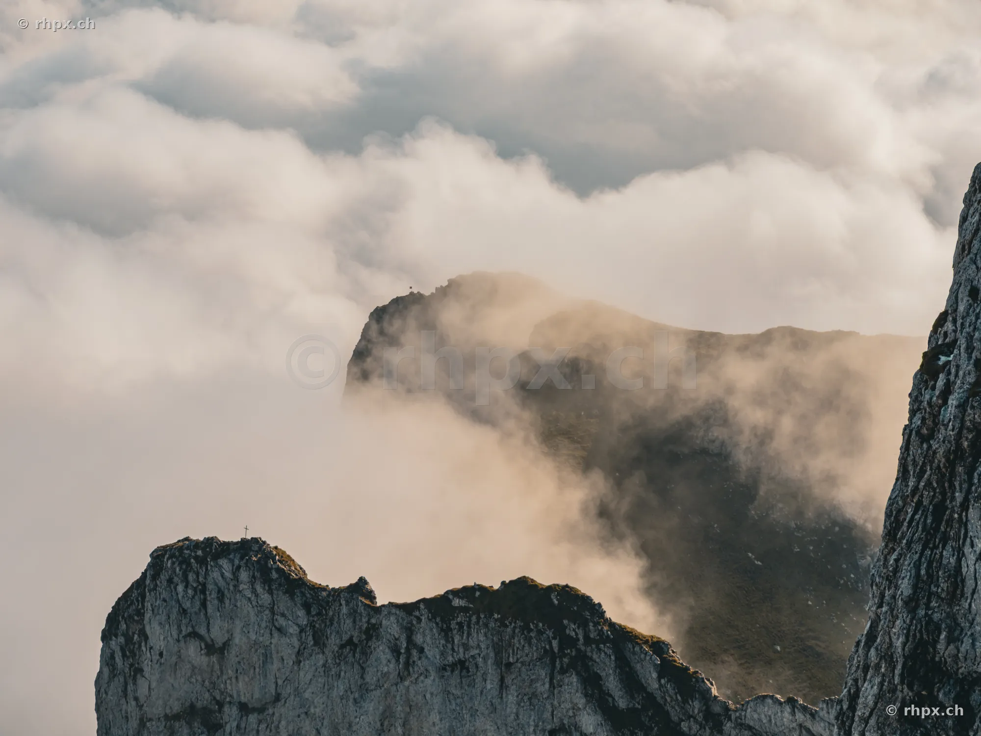 Blick auf die schroffen Felsen des Pilatus, die aus einer dichten Wolkendecke herausragen.
