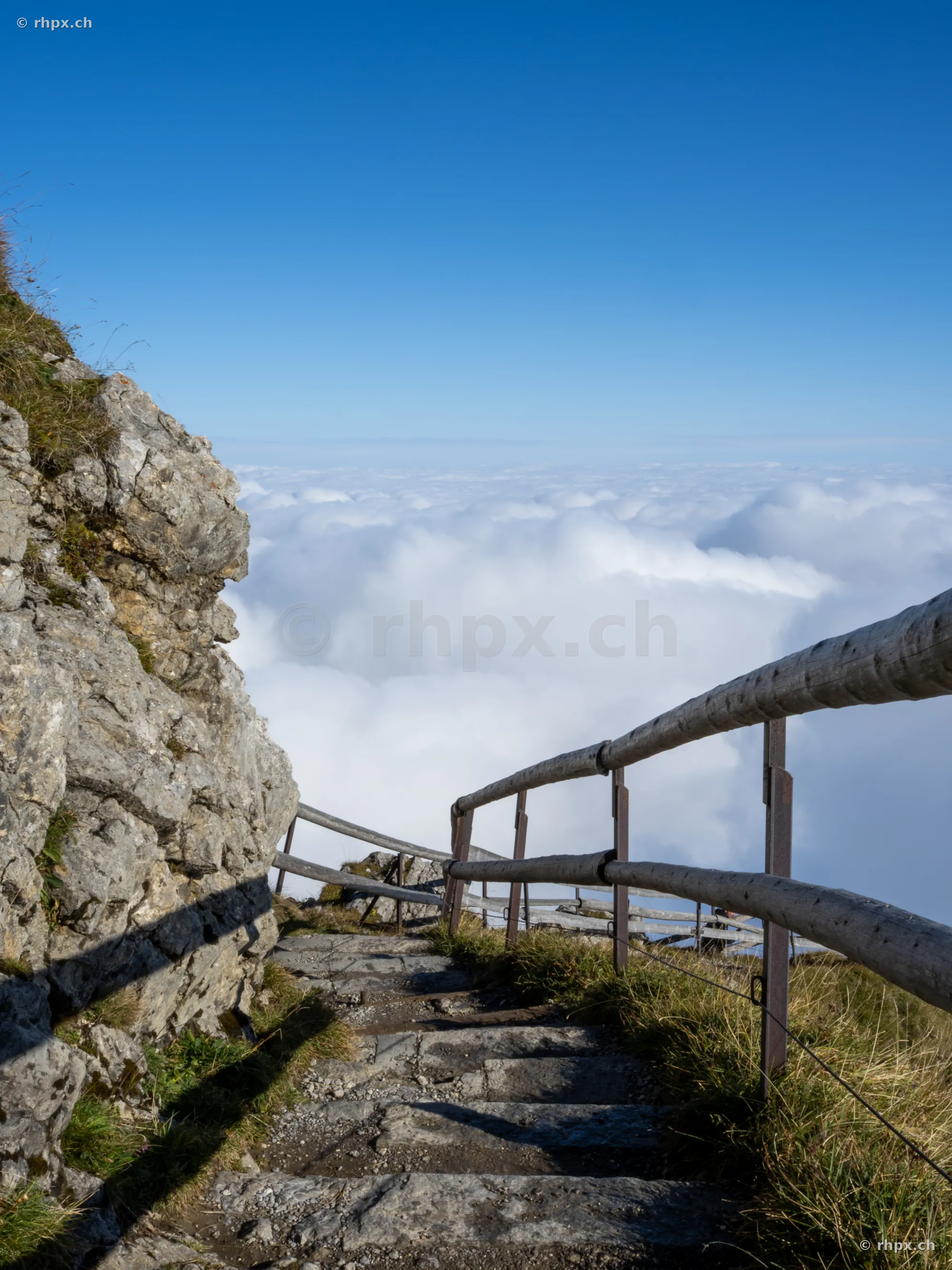 Steep stone stairs with wooden railing on Mount Pilatus above a thick cloud cover