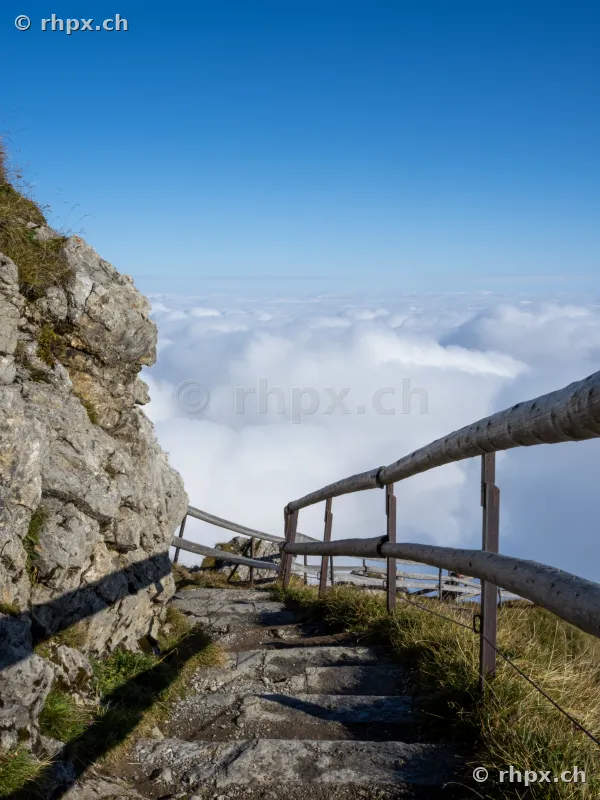 Steep stone stairs with wooden railing on Mount Pilatus above a thick cloud cover