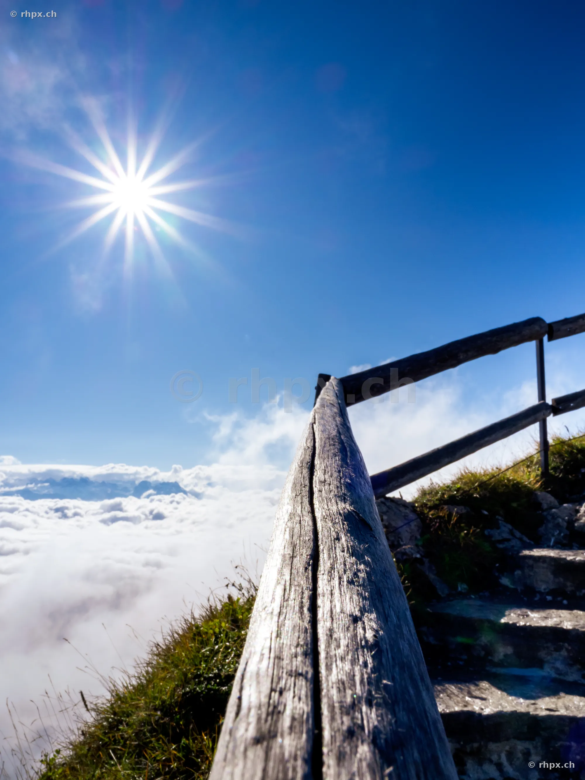 Wooden railing and stairs on Mount Pilatus overlooking a sea of clouds in bright sunshine