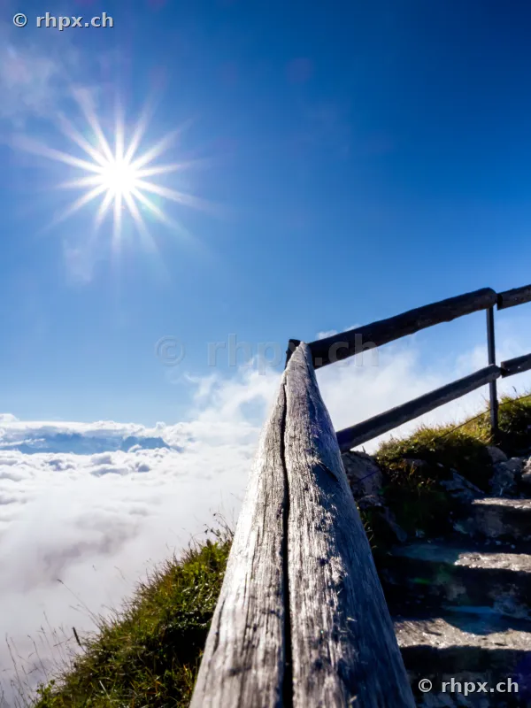 Wooden railing and stairs on Mount Pilatus overlooking a sea of clouds in bright sunshine