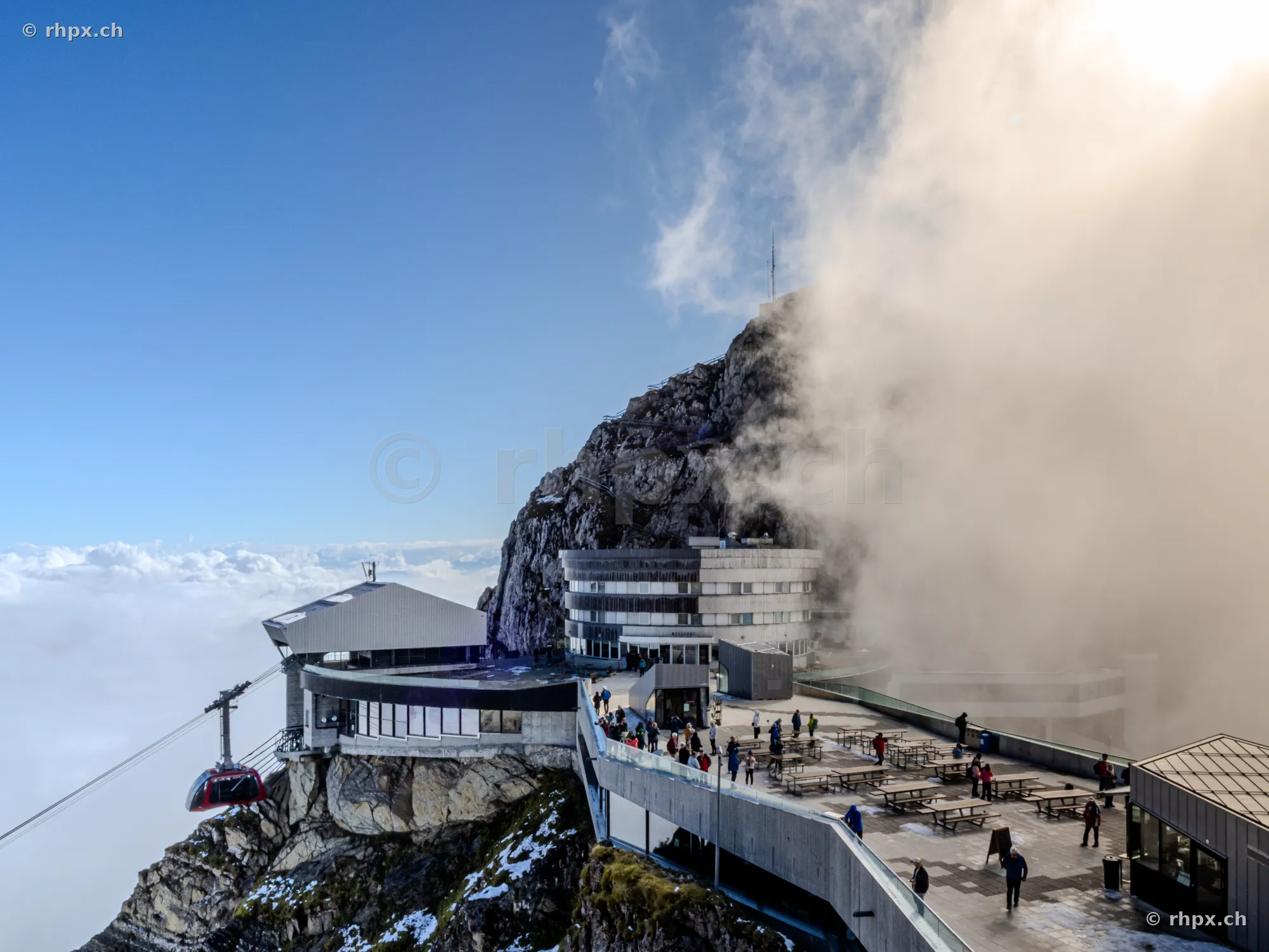 View of the Pilatus Kulm hotel and arriving cable car under a partially cloudy sky.