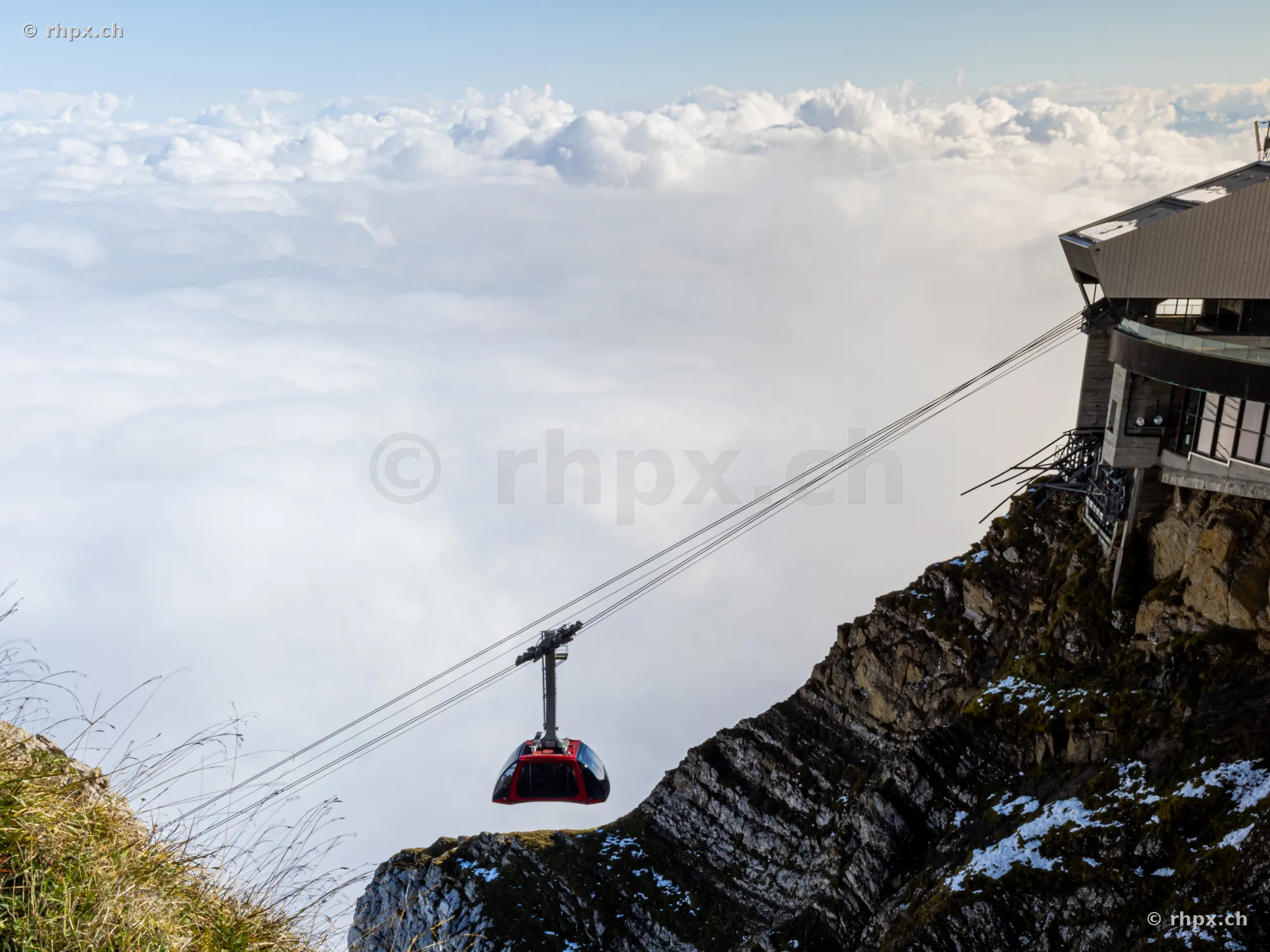 Rote Luftseilbahn vor der Bergstation des Pilatus über einer dichten Wolkendecke